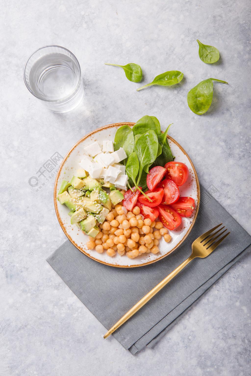 有鱷梨、鷹嘴豆、菲塔芝士、新鮮菠菜、番茄和一杯水的佛碗。 健康素食排毒均衡膳食的概念